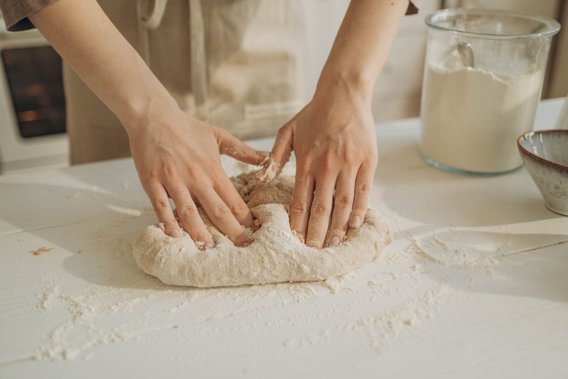 Hands kneading dough on a floured white table.