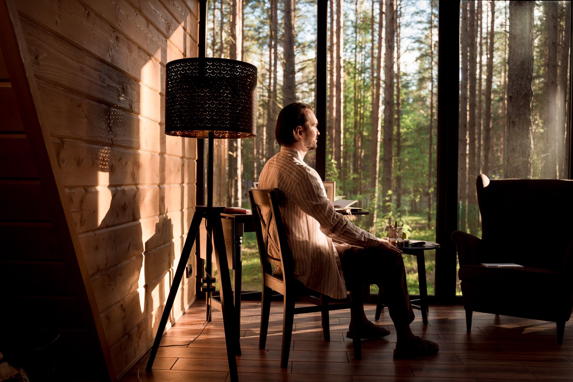 A man sitting in a forest cabin, looking out at the trees.