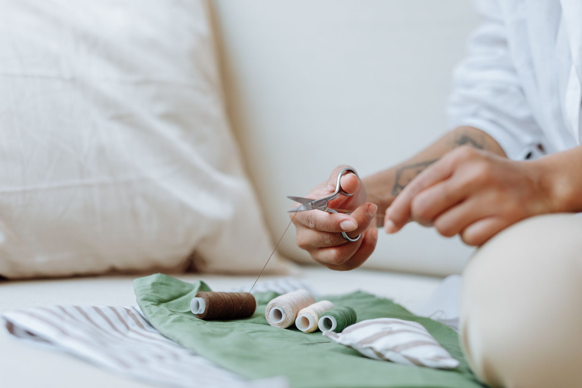 Close-up of hands sewing with threads, scissors, and fabric on a light surface.