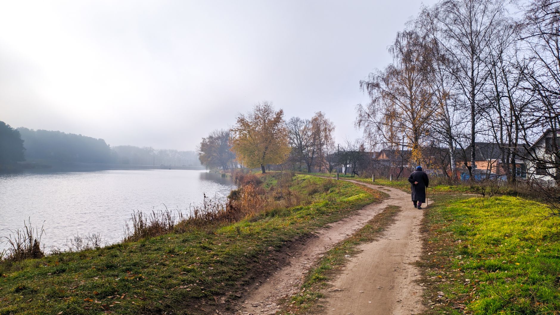 A solitary person walking a riverside path on a quiet autumn morning.